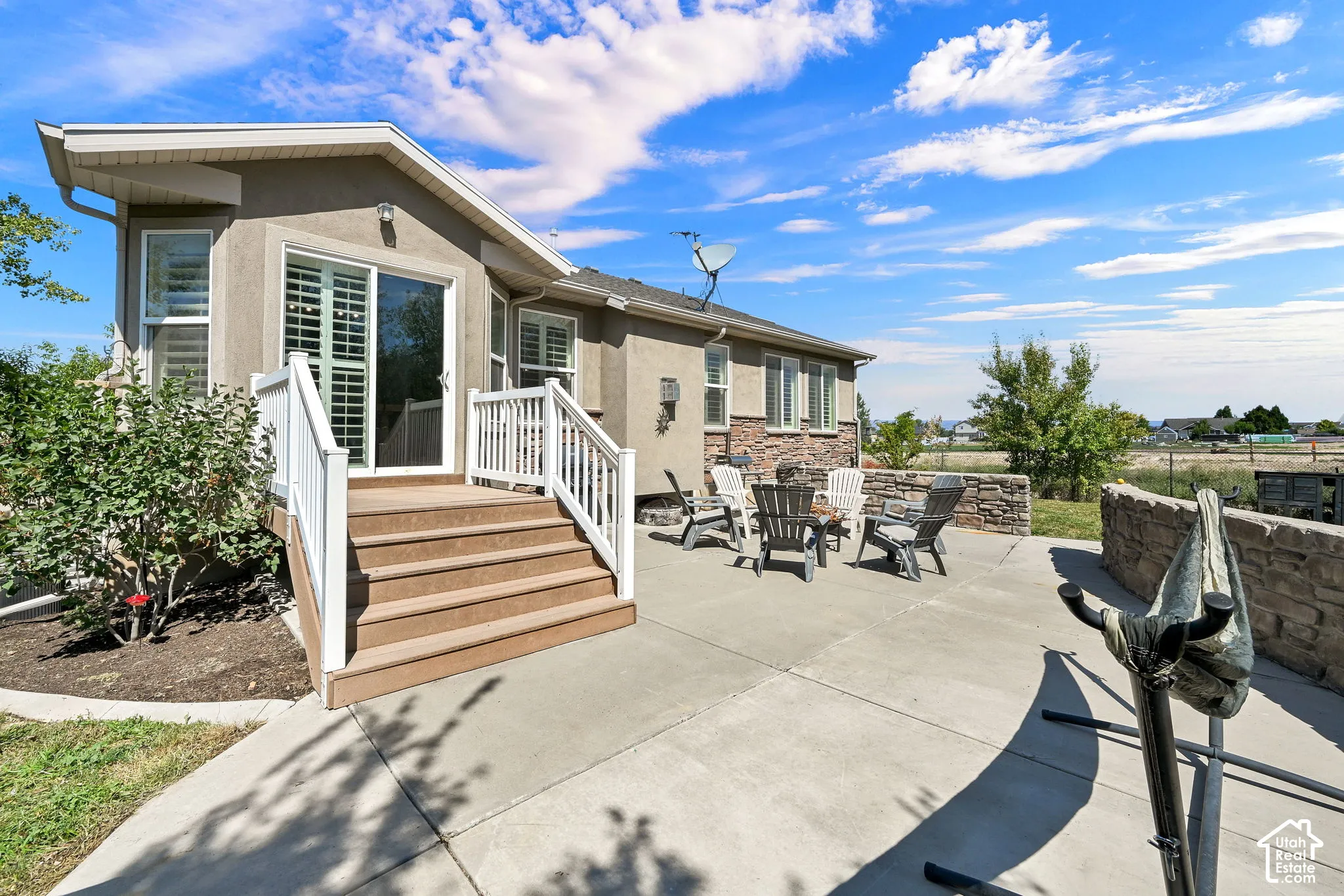 Rear exterior with a concrete patio, stone accent wall, and multi-level deck featuring white railings and composite steps