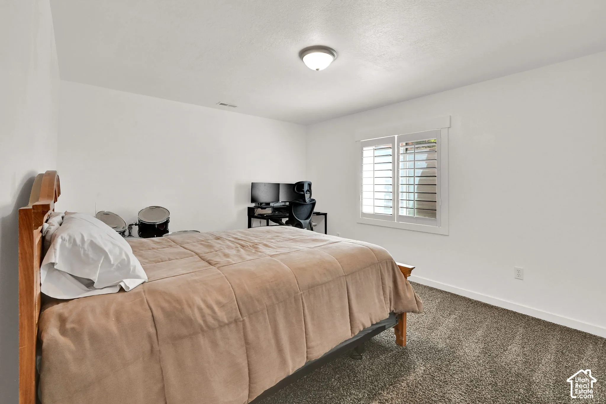 White walls with trim detail, a single window with plantation shutters, ceiling-mounted light fixture, and textured carpet flooring