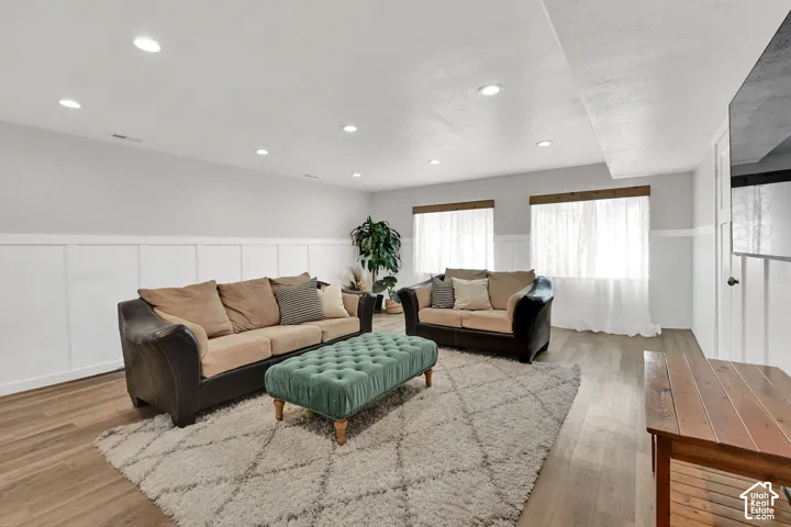 Recessed ceiling lighting, wood-finish flooring, white paneling, and two windows with wood trim