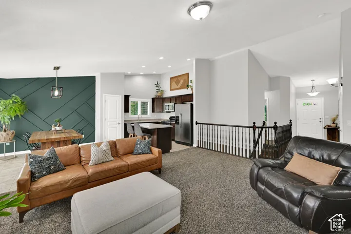 Open-concept living space featuring a distinct dining area with a geometric accent wall, kitchen with stainless steel appliances, and a staircase with a white spindle railing