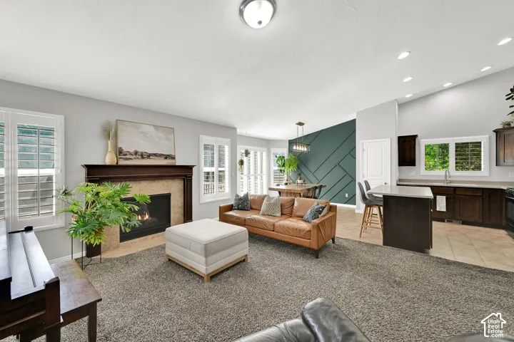 Open-concept living space featuring a fireplace with a wood mantel, plantation shutters, vaulted ceilings, a kitchen island with seating, and dark wood cabinetry