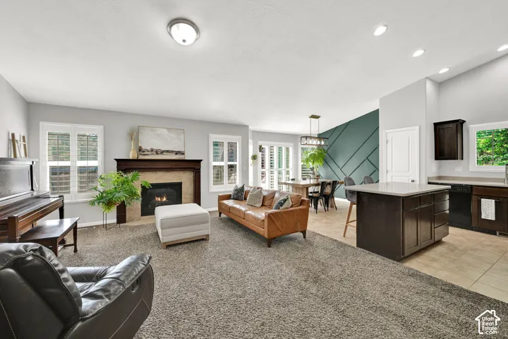 Fireplace with a wood mantle, carpeted living area, kitchen island with countertop seating, tiled kitchen flooring, and a unique accent wall