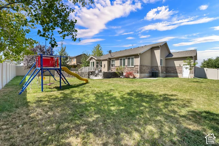 Expansive rear yard featuring a manicured lawn, established privacy fencing, and a stucco exterior with stone veneer accents