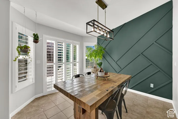 Accent wall with geometric paneling, bay windows with plantation shutters, tile flooring, and a linear pendant light fixture