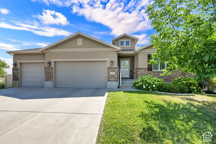 Stucco exterior with stone accents, two-car garage, concrete driveway, front entry porch, and established landscaping