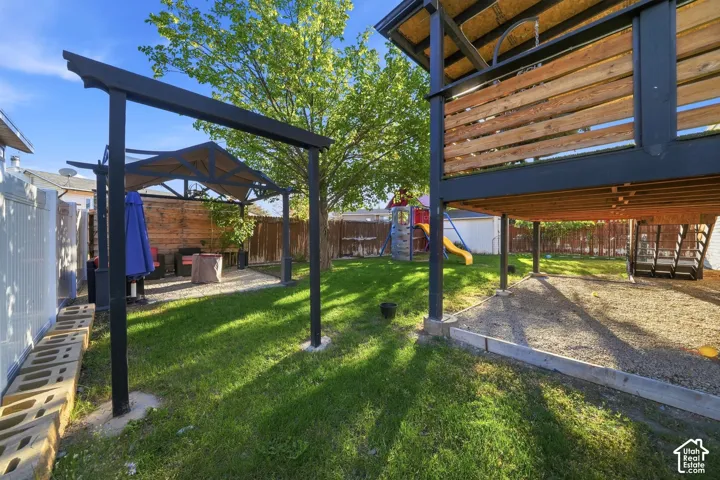 Expansive backyard featuring a manicured lawn, a raised wood and metal deck structure, a gravel-covered area under the deck, and an additional gravel patio with a pergola