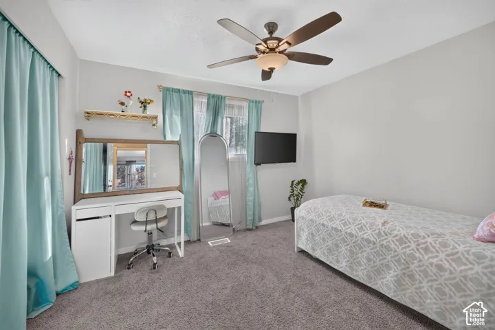 Wall-mounted television, ceiling fan with integrated lighting, and neutral-toned carpeting