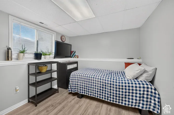Recessed window with blinds, wood-finish flooring, drop ceiling with fluorescent lighting, and two-tone wall paint