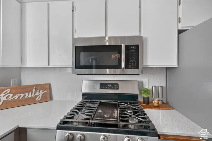 Stainless steel over-the-range microwave, gas range with griddle, light-toned countertops, and white upper cabinetry