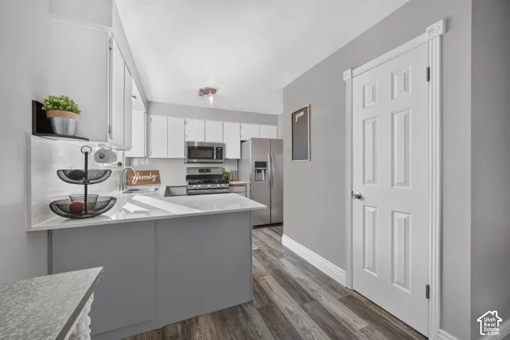 White cabinetry, stainless steel appliances, wood-finish flooring, white countertops, and decorative door trim