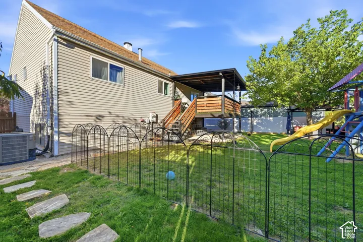 Expansive backyard featuring a covered deck, wood privacy fencing, and a grass lawn with stepping stones
