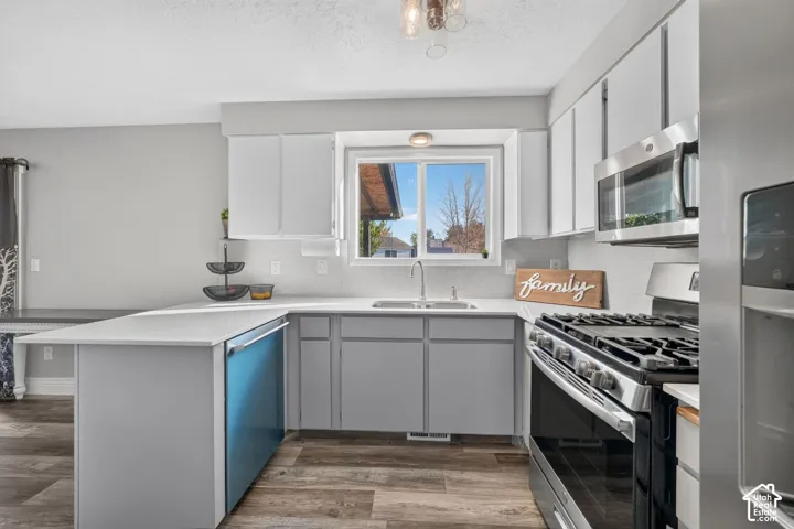 Kitchen featuring white upper cabinetry, gray lower cabinetry, stainless steel appliances, wood-finish flooring, and light countertops with a tile backsplash