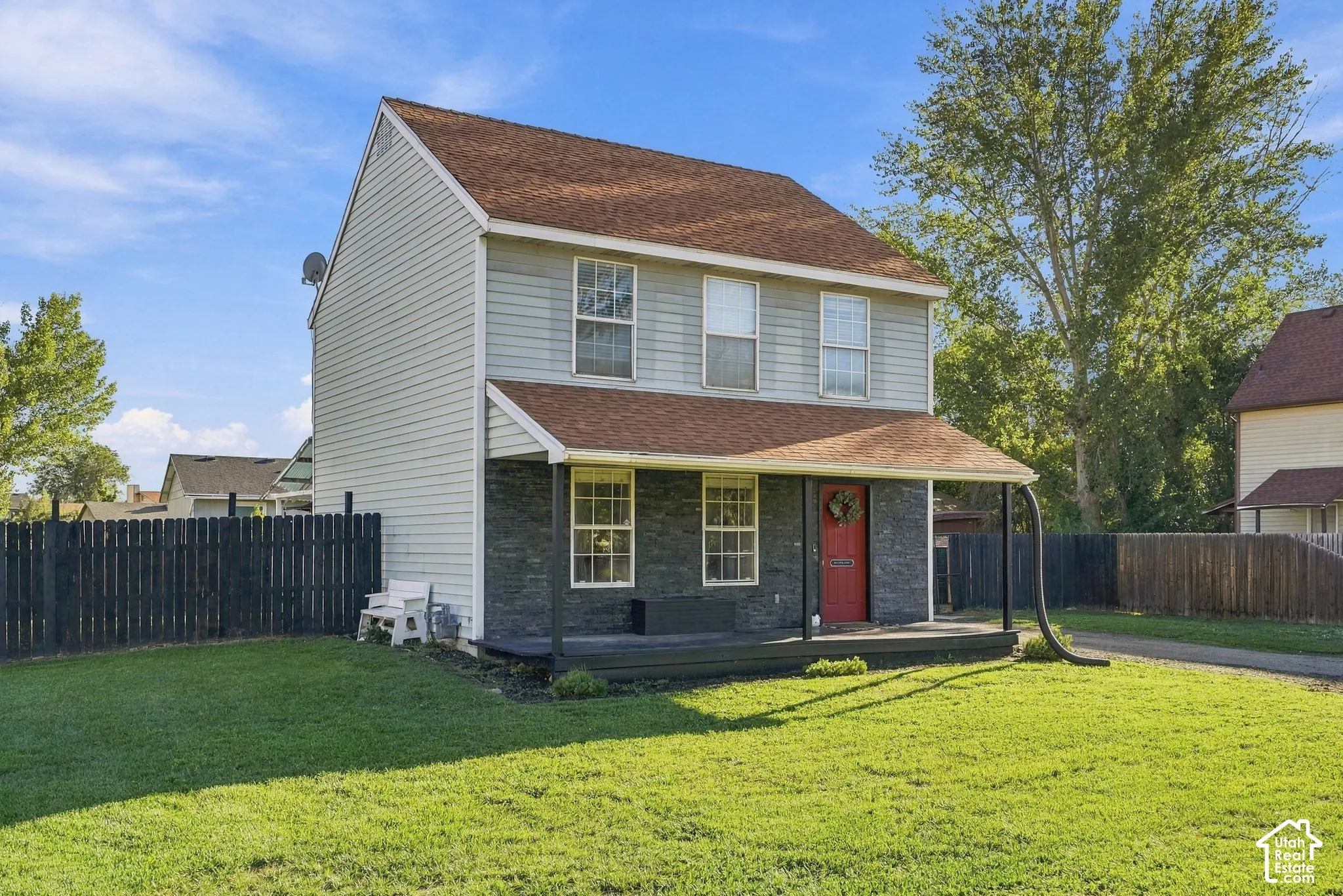 Two-story residence with a covered porch, red entry door, shingle roof, and a fenced yard