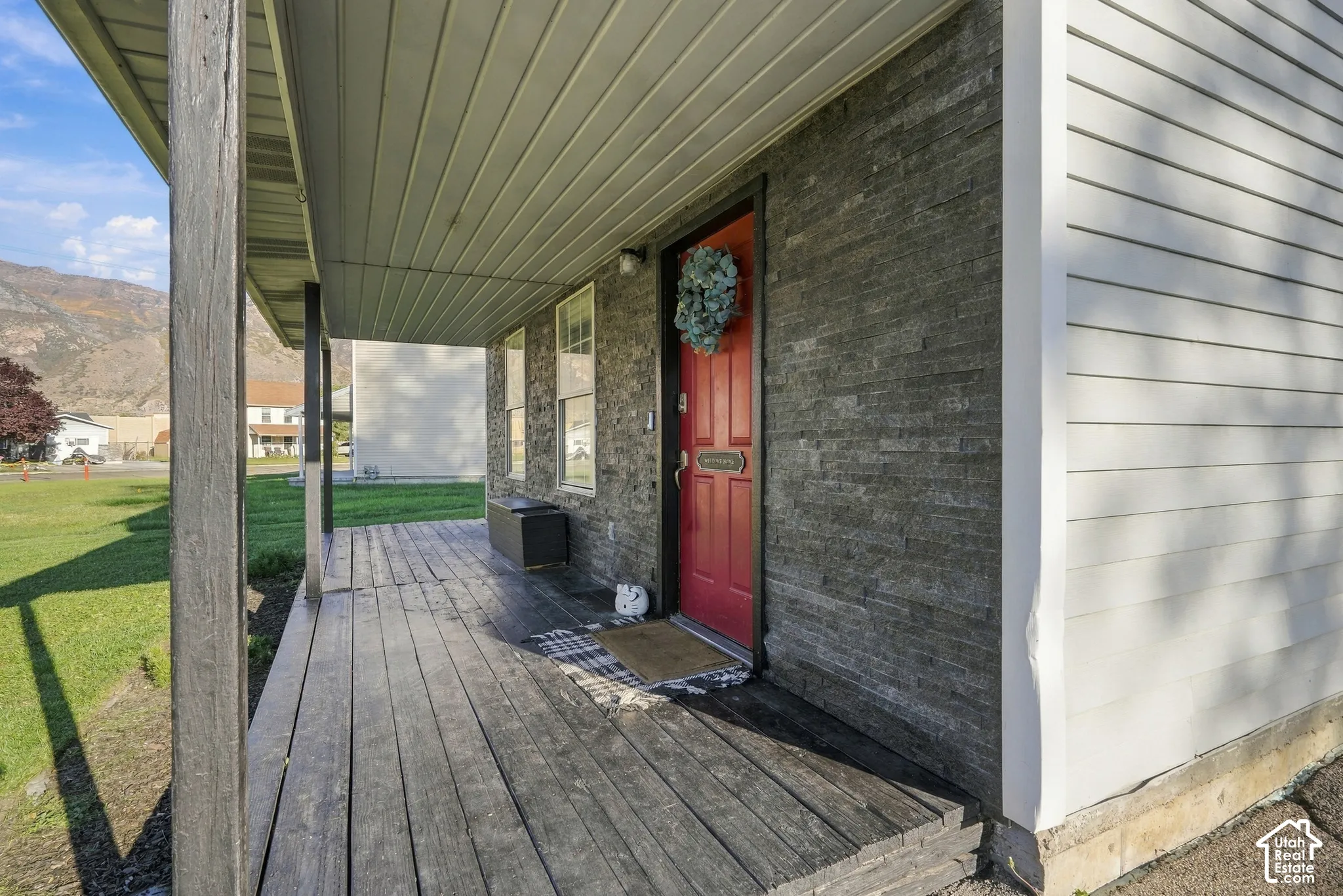 Expansive covered front porch with wood-finish decking, dark wood support columns, stone veneer accent wall, and a bright red front door