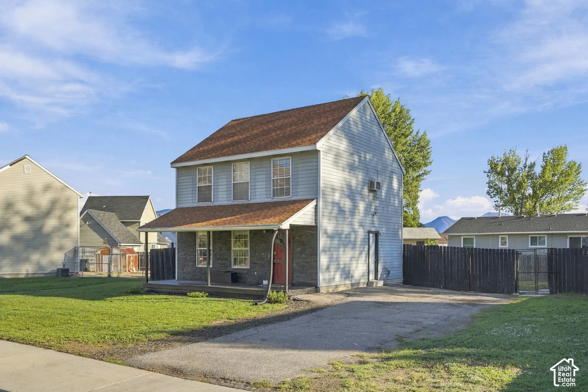 Two-story residence with light blue siding, brown shingle roof, covered front porch, and an attached paved driveway