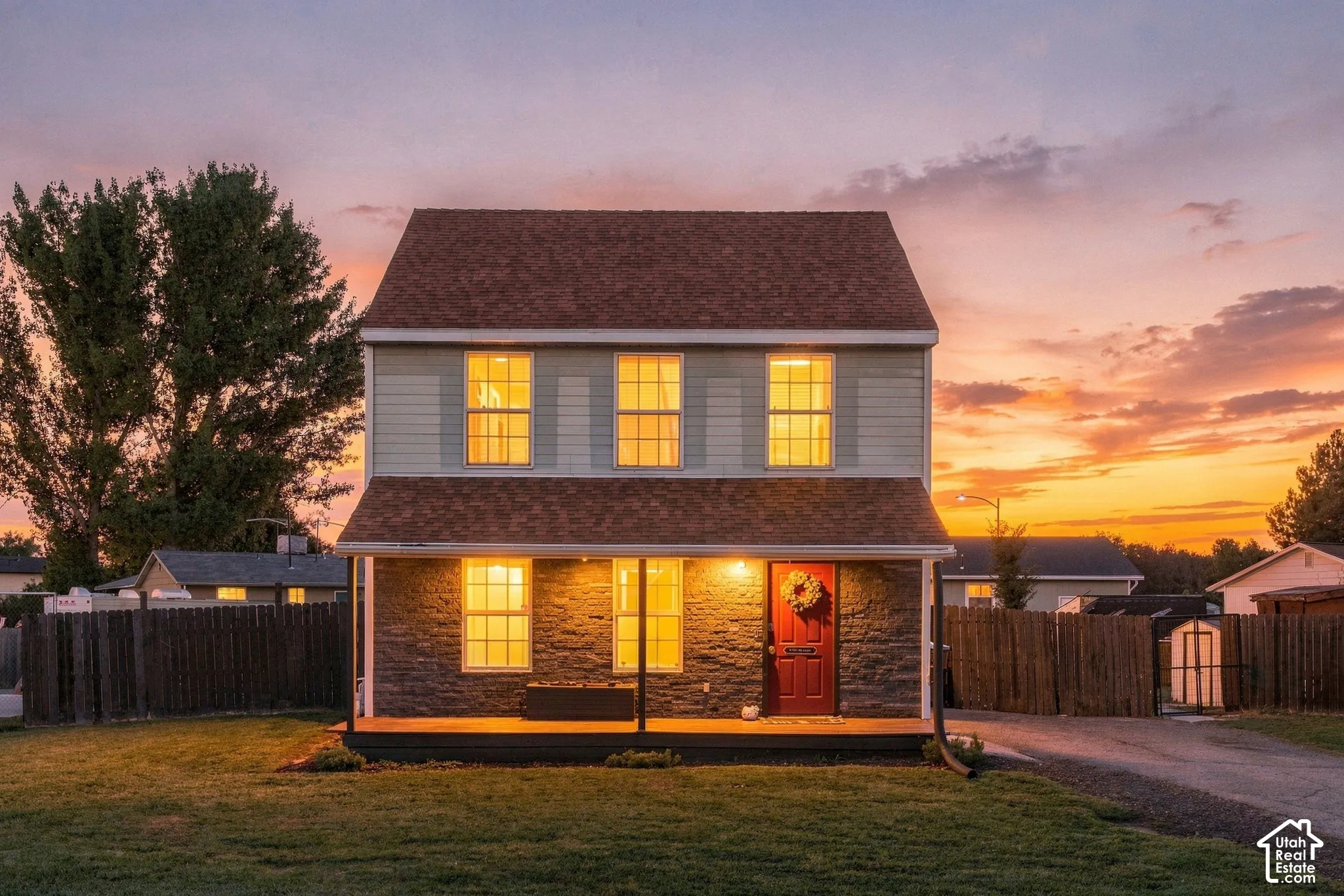 Two-story residence with a covered porch, stone-finish lower facade, light-colored upper siding, and a prominent red entry door