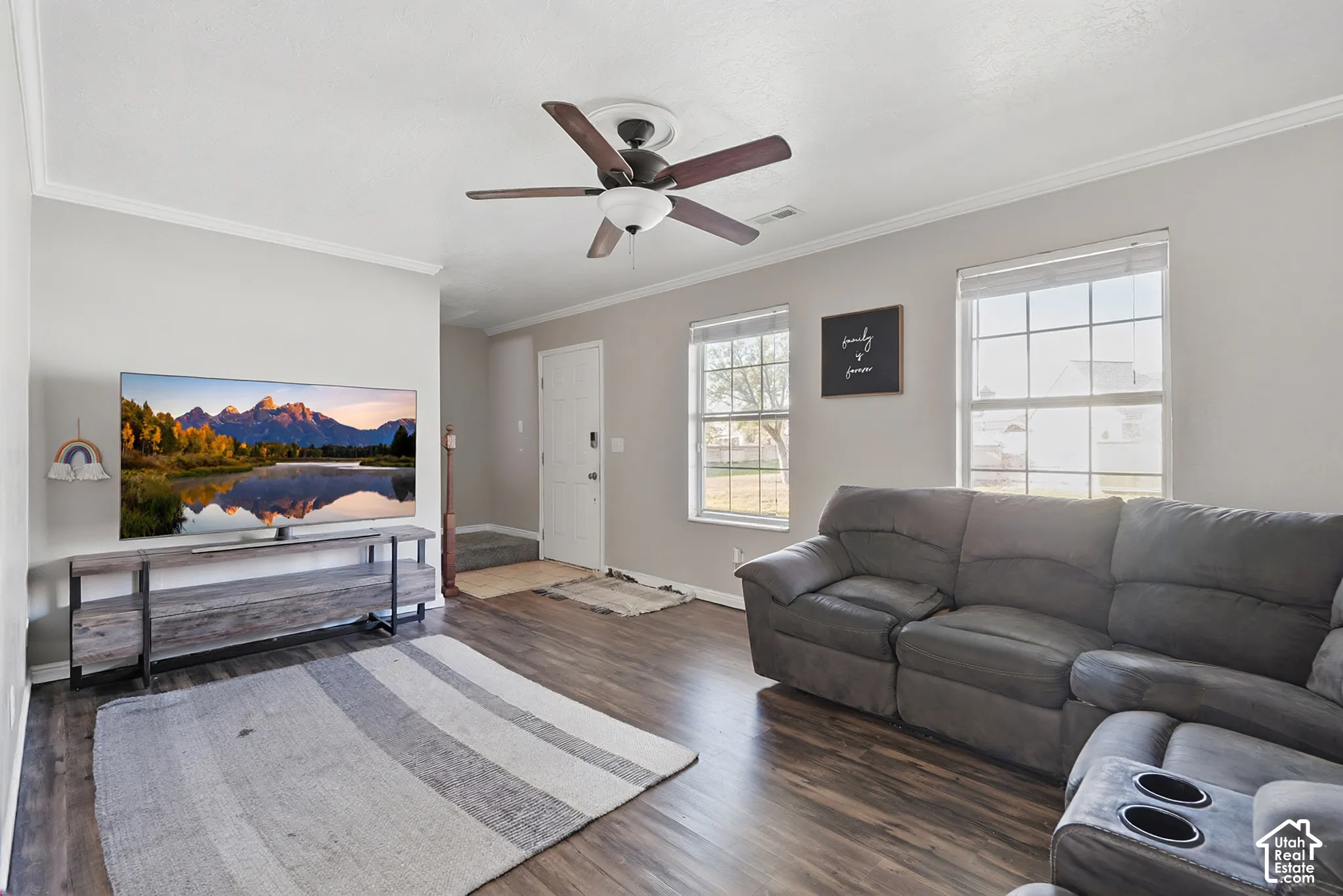 Wood-finish flooring, two large windows, white trim, and a ceiling fan with integrated lighting