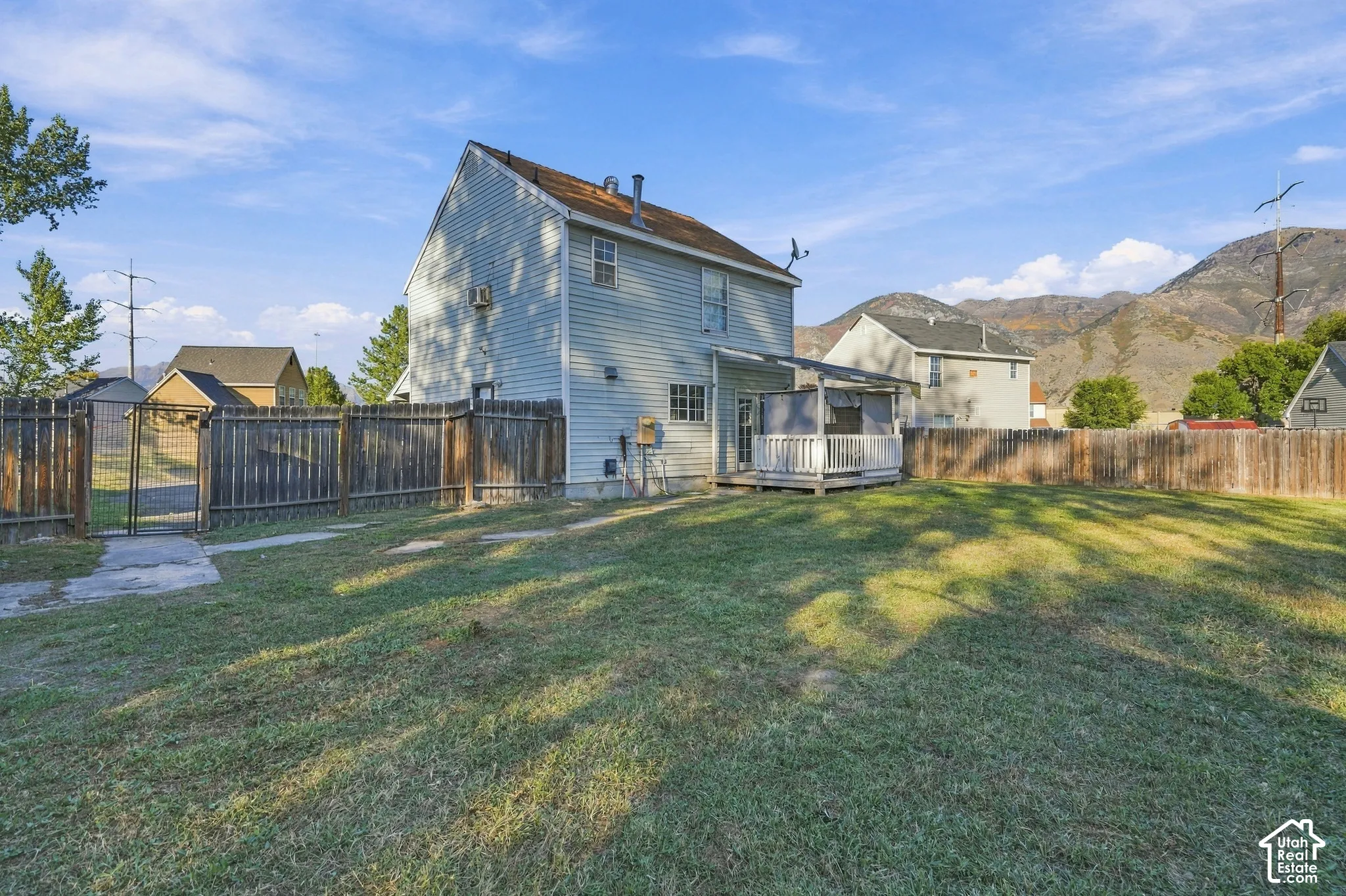 Expansive fenced yard with a gate, featuring a covered deck and a two-story residence with siding