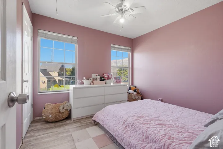 Room with wood-finish flooring, two large windows, and a ceiling fan with integrated lighting