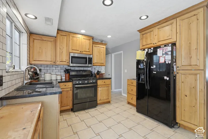 Kitchen featuring wood cabinetry, stainless steel microwave, black range, black side-by-side refrigerator, and tile flooring
