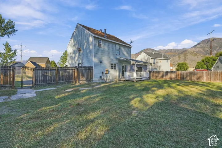 Expansive fenced yard with a gate, featuring a covered deck and a two-story residence with siding
