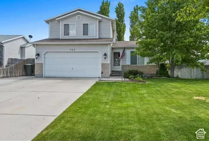 Two-story exterior with light-colored siding, attached garage, concrete driveway, front lawn, and mature tree