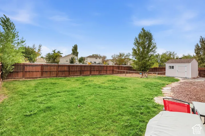 Expansive backyard featuring a manicured lawn, a brown privacy fence, a storage shed, and a stone-path leading to a mulched area