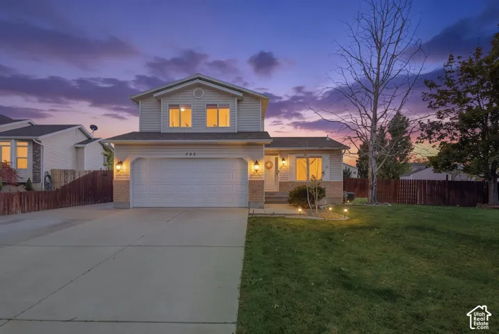 Two-story property featuring a front-facing garage with a concrete driveway, a manicured lawn, and exterior wall sconces