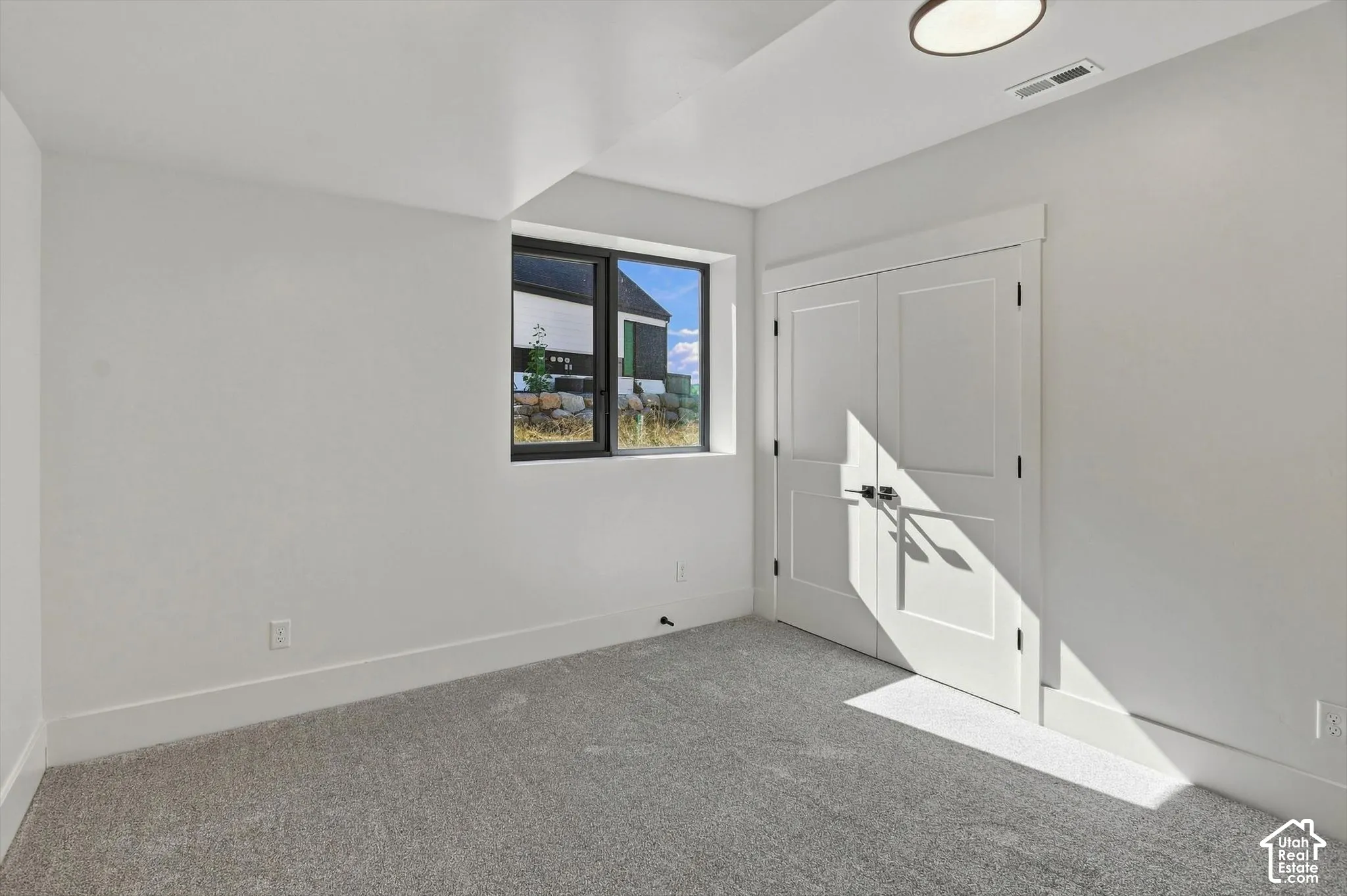 Recessed window with black trim, white interior walls, light gray carpeting, and a built-in closet with white bifold doors