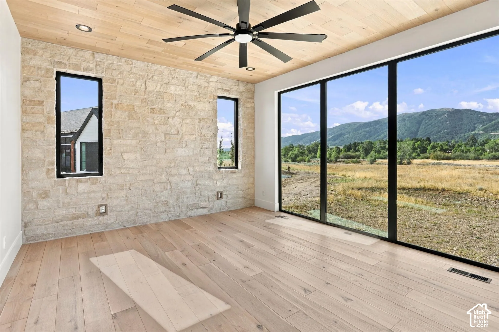 Stone-clad accent wall with recessed lighting, wood-finish flooring, full-height window wall, wood-paneled ceiling, and a ceiling fan