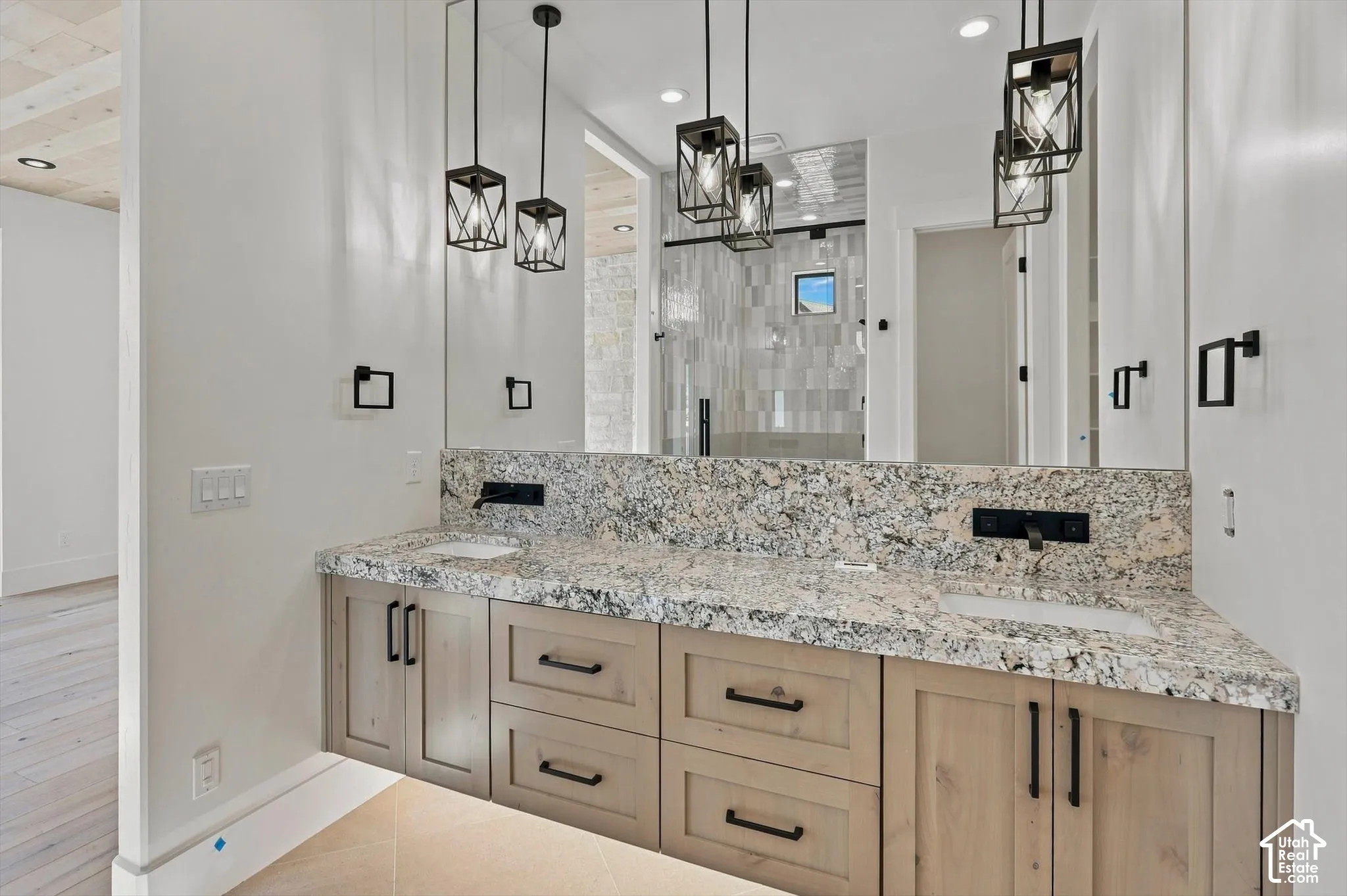 Dual vanity with granite countertop and integrated sinks, wall-mounted matte black faucets, and dark-framed pendant lighting