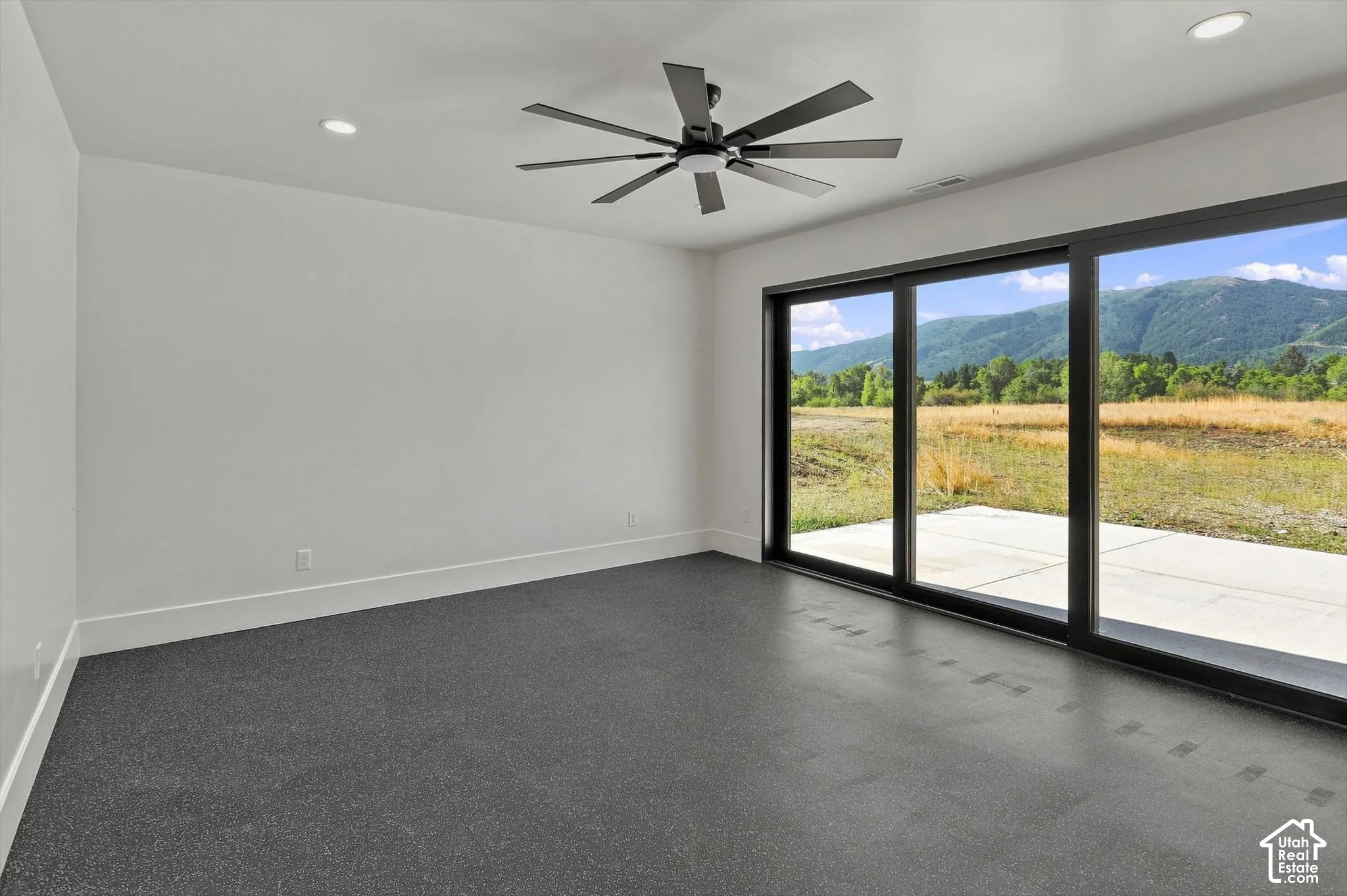 Expansive sliding glass doors, dark flooring, recessed ceiling lighting, ceiling fan with black finish, and a concrete patio