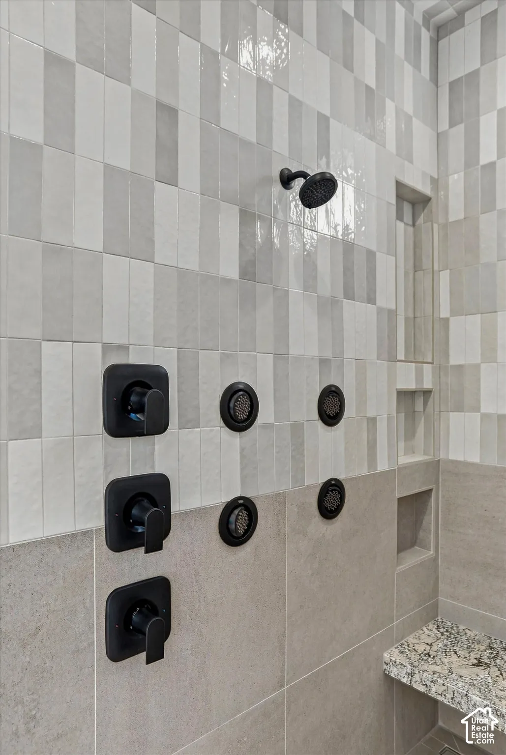 Tiled shower with matte black fixtures, multiple body sprays, built-in shower niches, and a stone-finish bench