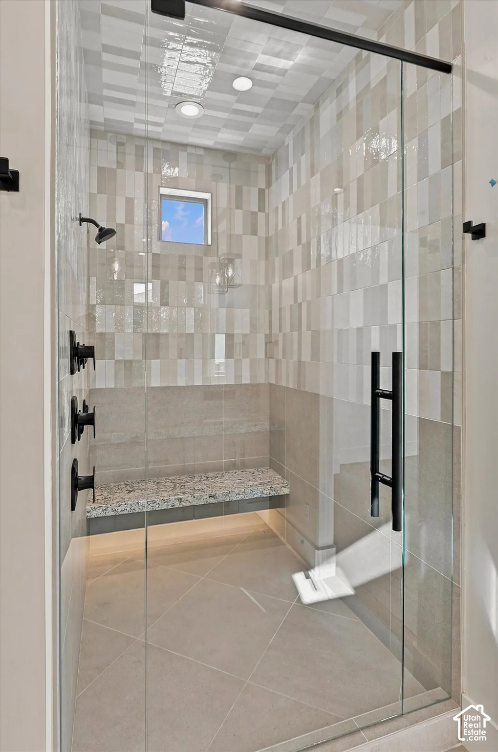 Walk-in shower with clear glass enclosure, matte black fixtures, integrated window, tiled walls, and a built-in stone bench
