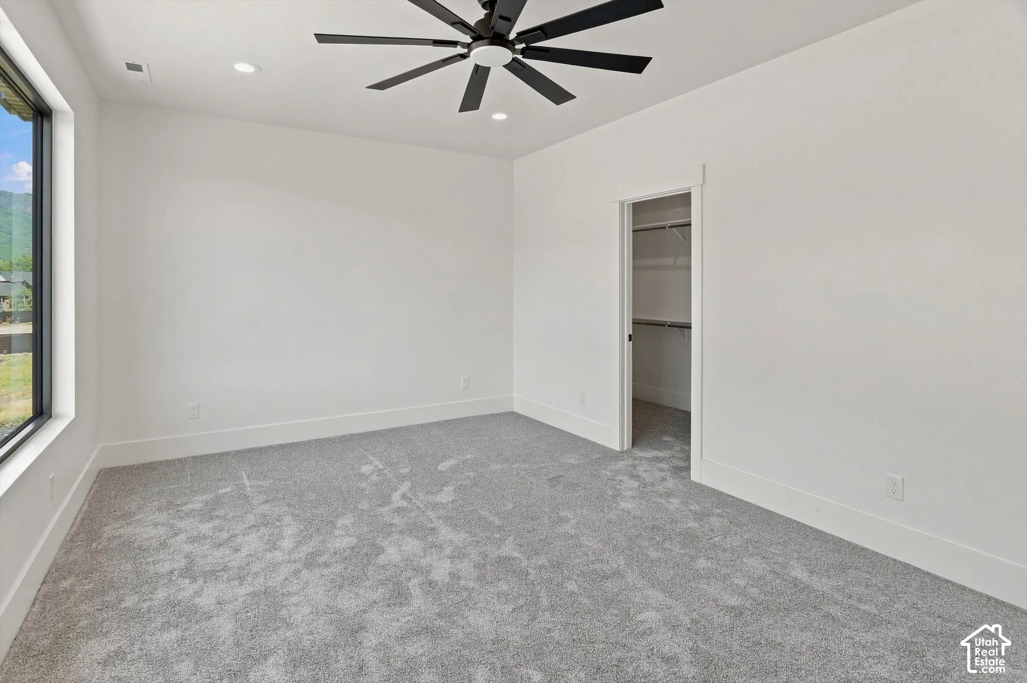Spacious room featuring a contemporary ceiling fan, recessed lighting, expansive window, closet with built-in shelving, and light gray carpeting