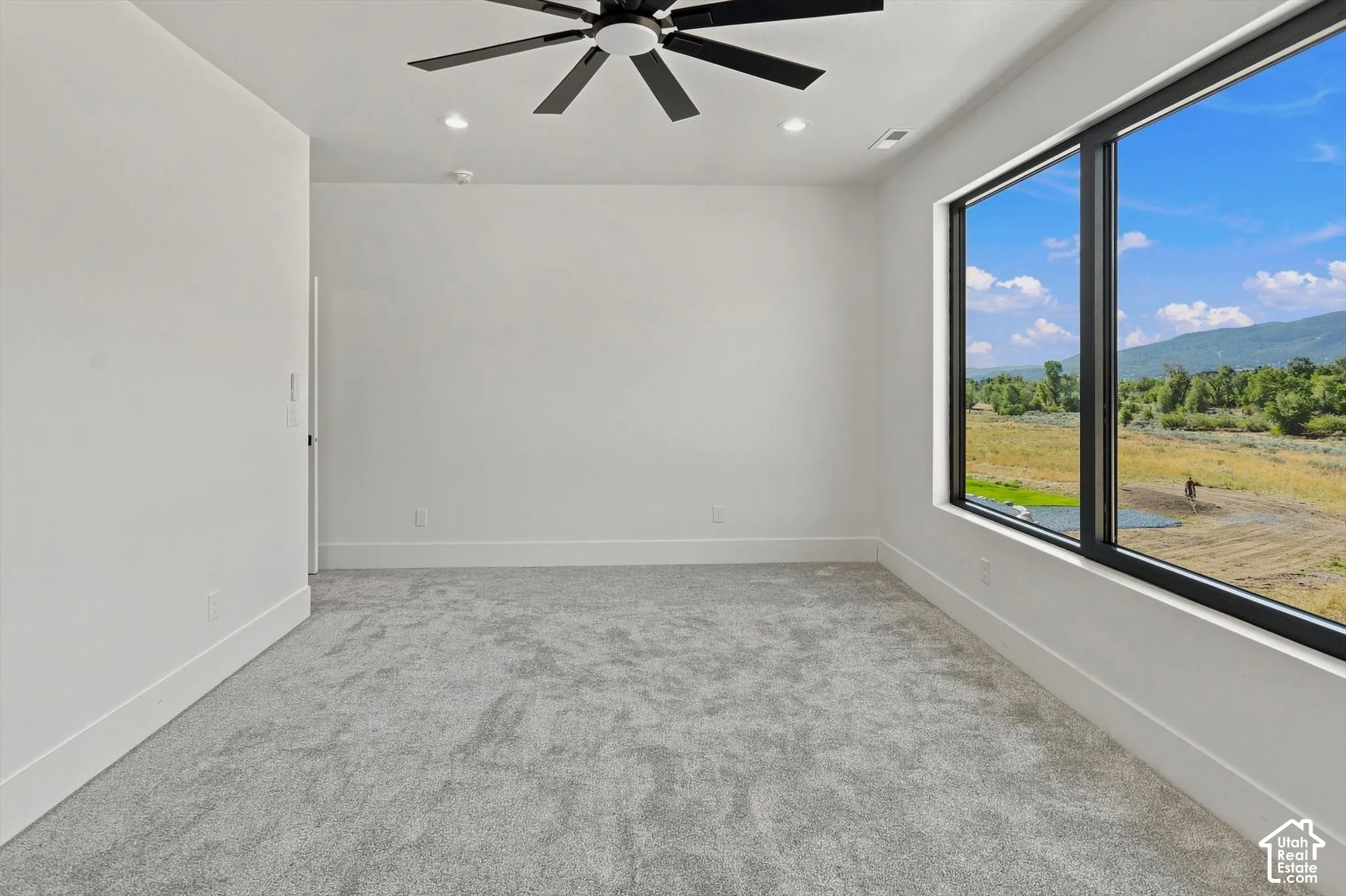 Recessed lighting, ceiling fan, expansive window, mountain scenery, and grey carpet flooring
