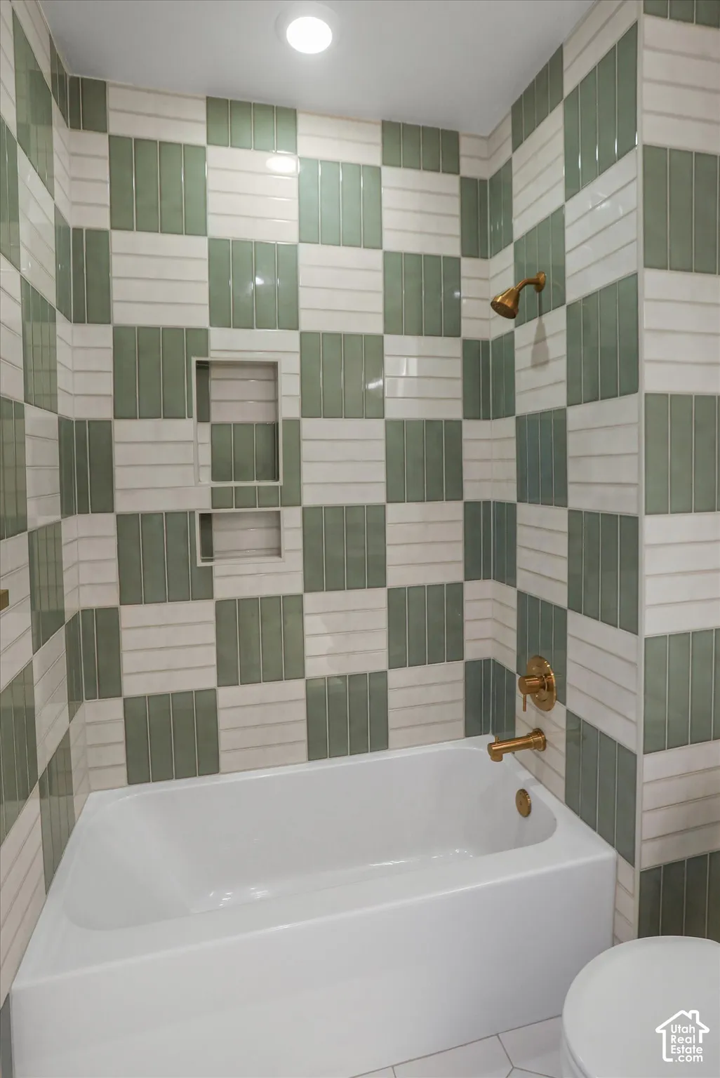 Bathtub with gold-tone fixtures, tiled shower surround, recessed shower niches, and recessed lighting
