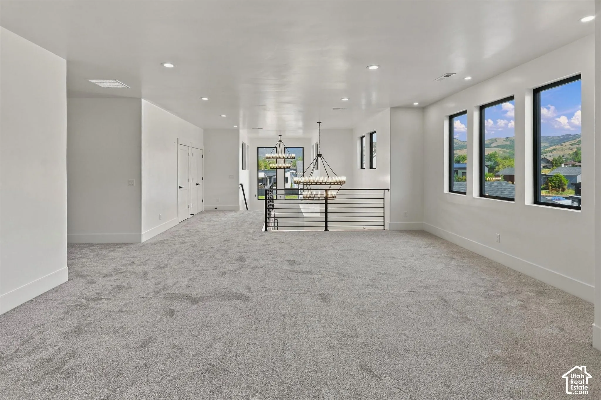 Recessed lighting, three large picture windows, contemporary black metal railing, and two tiered chandeliers