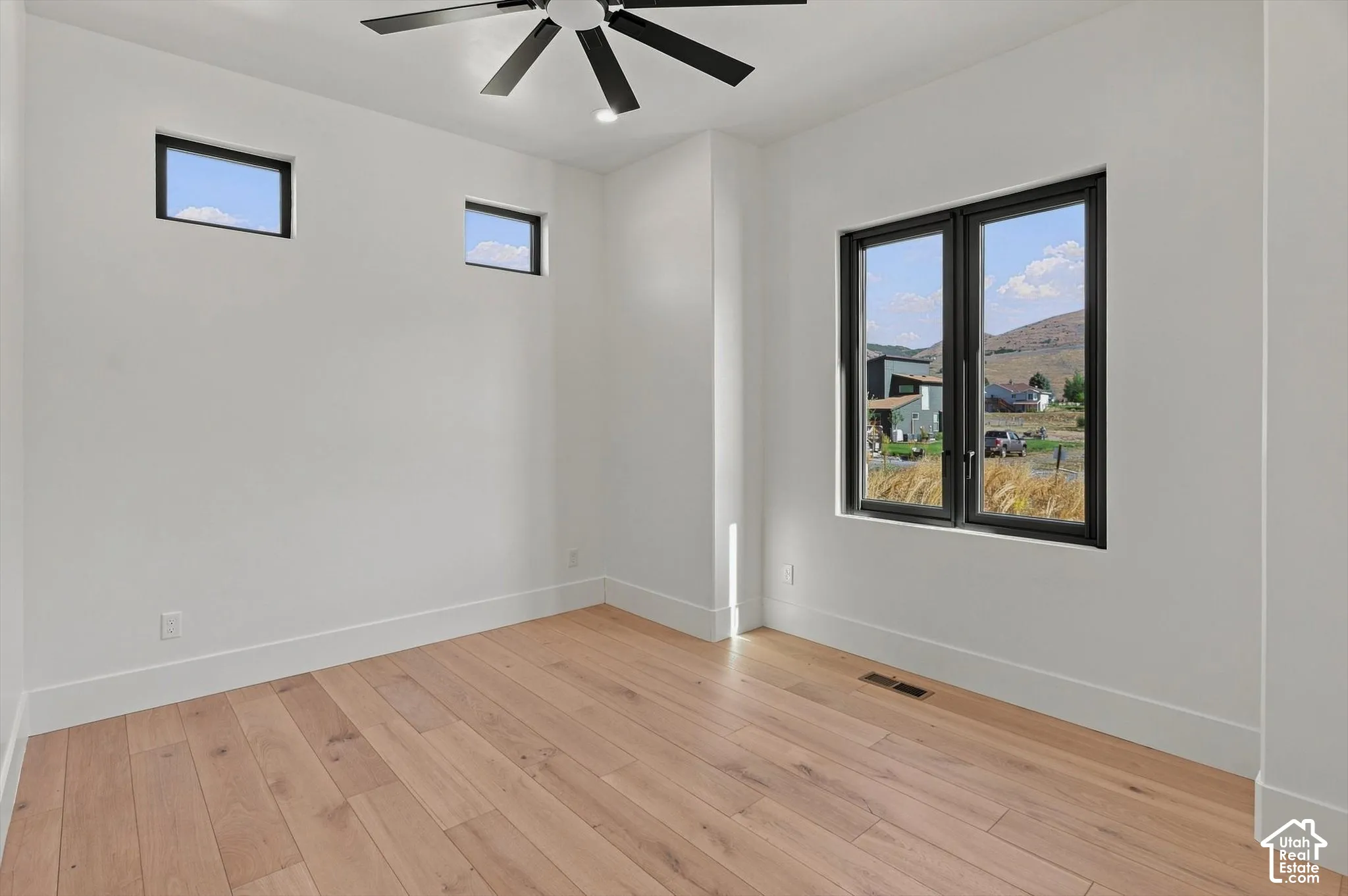 Wood-finish flooring, white walls, black-framed windows, and a black ceiling fan