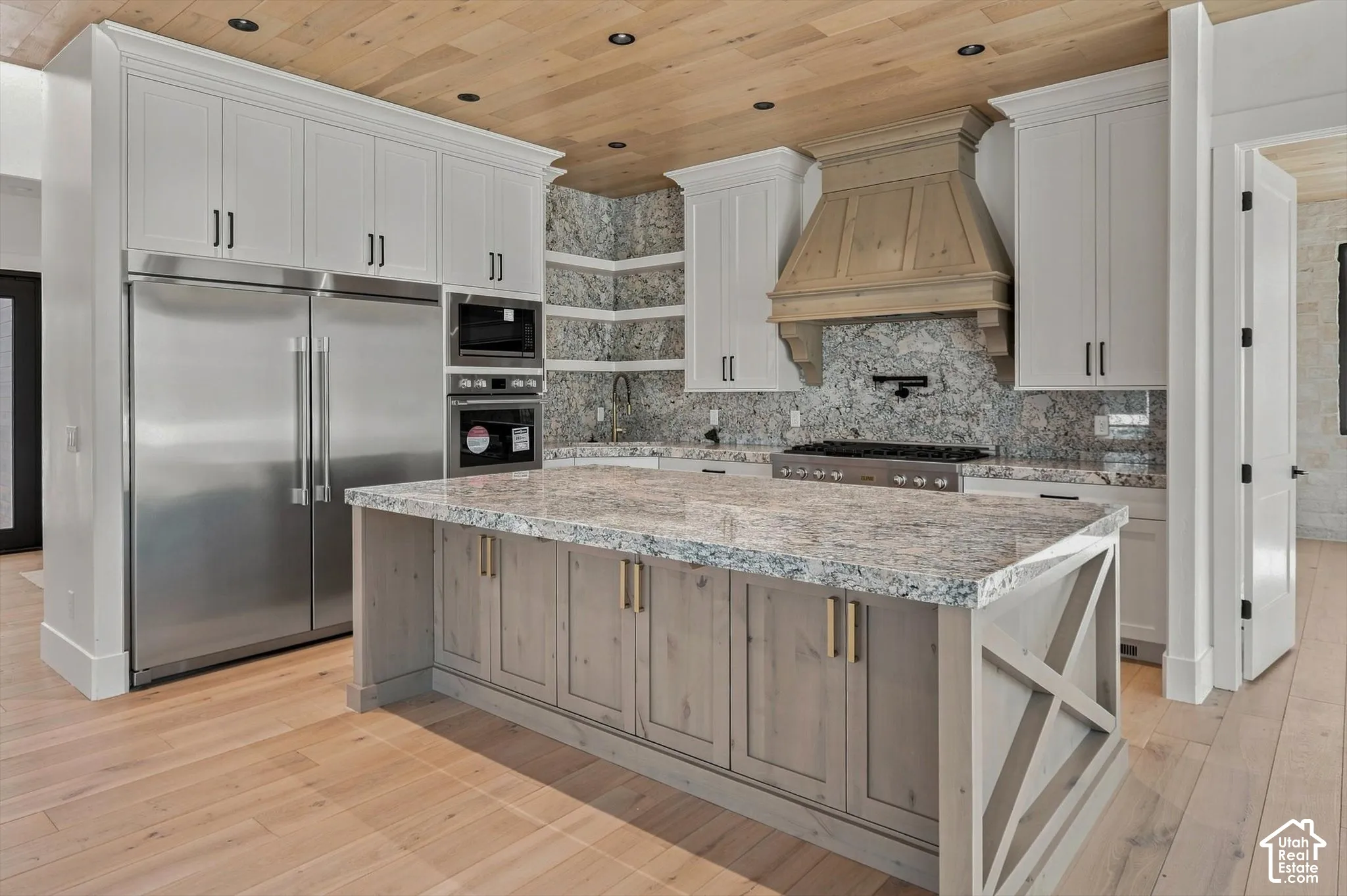 Gourmet kitchen featuring a large central island with light-toned cabinetry, stainless steel appliances, and a wood-finish ceiling