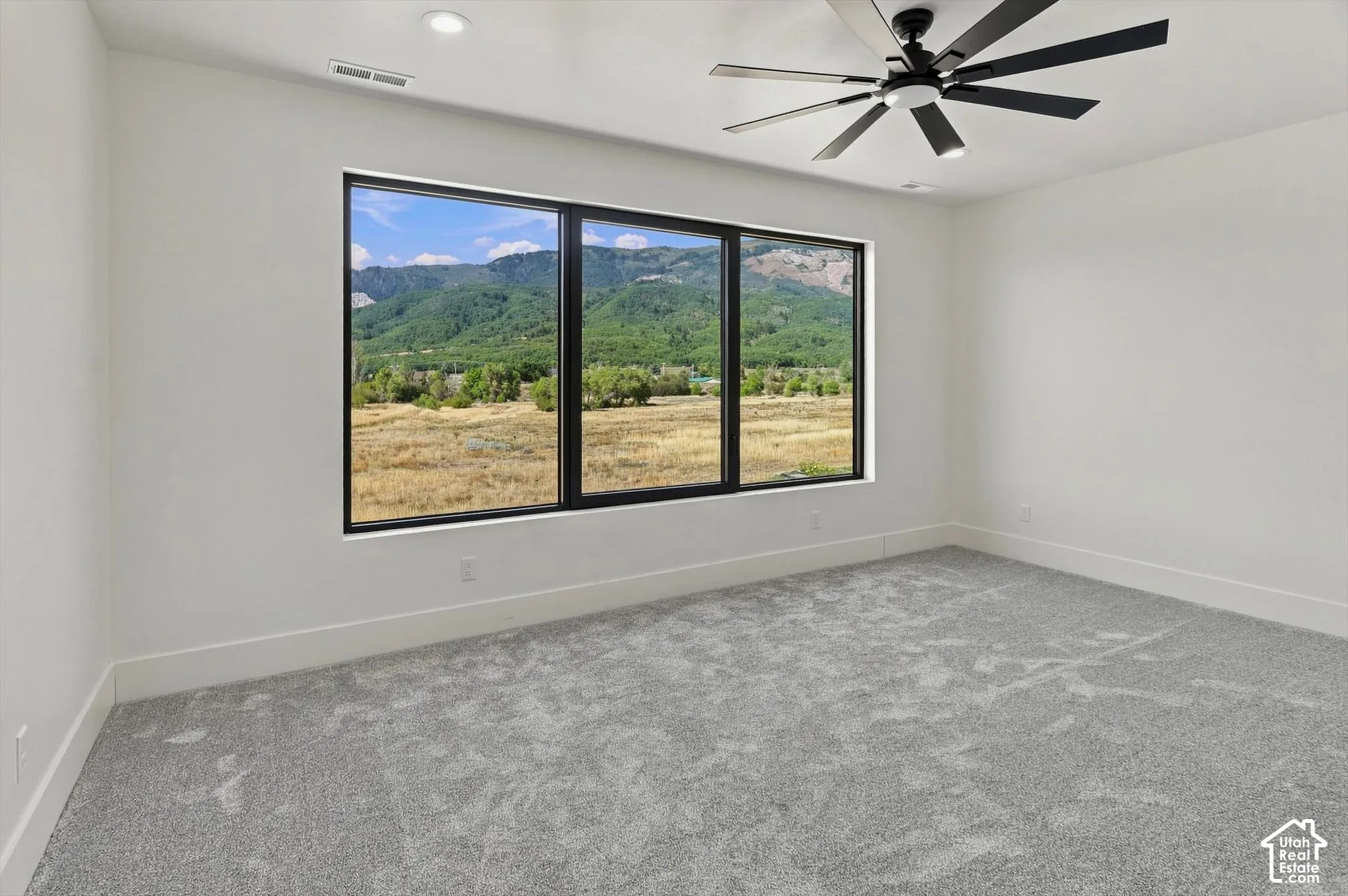 Expansive picture windows framing mountain scenery, modern ceiling fan with integrated lighting, recessed lighting, neutral wall finishes, and light-toned carpeting