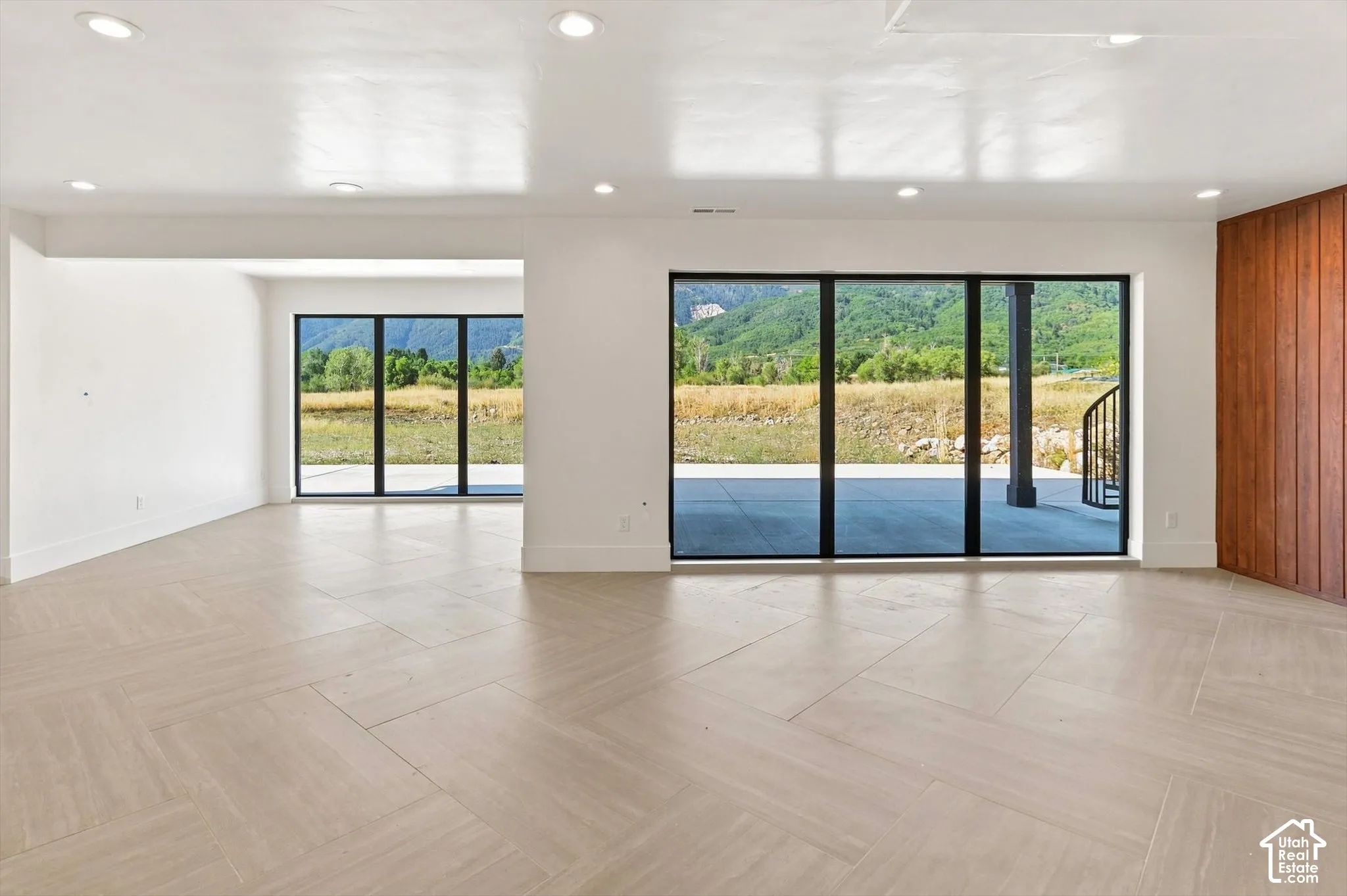 Recessed lighting, wood-finish flooring with a herringbone pattern, expansive sliding glass doors, and a wood-paneled accent wall