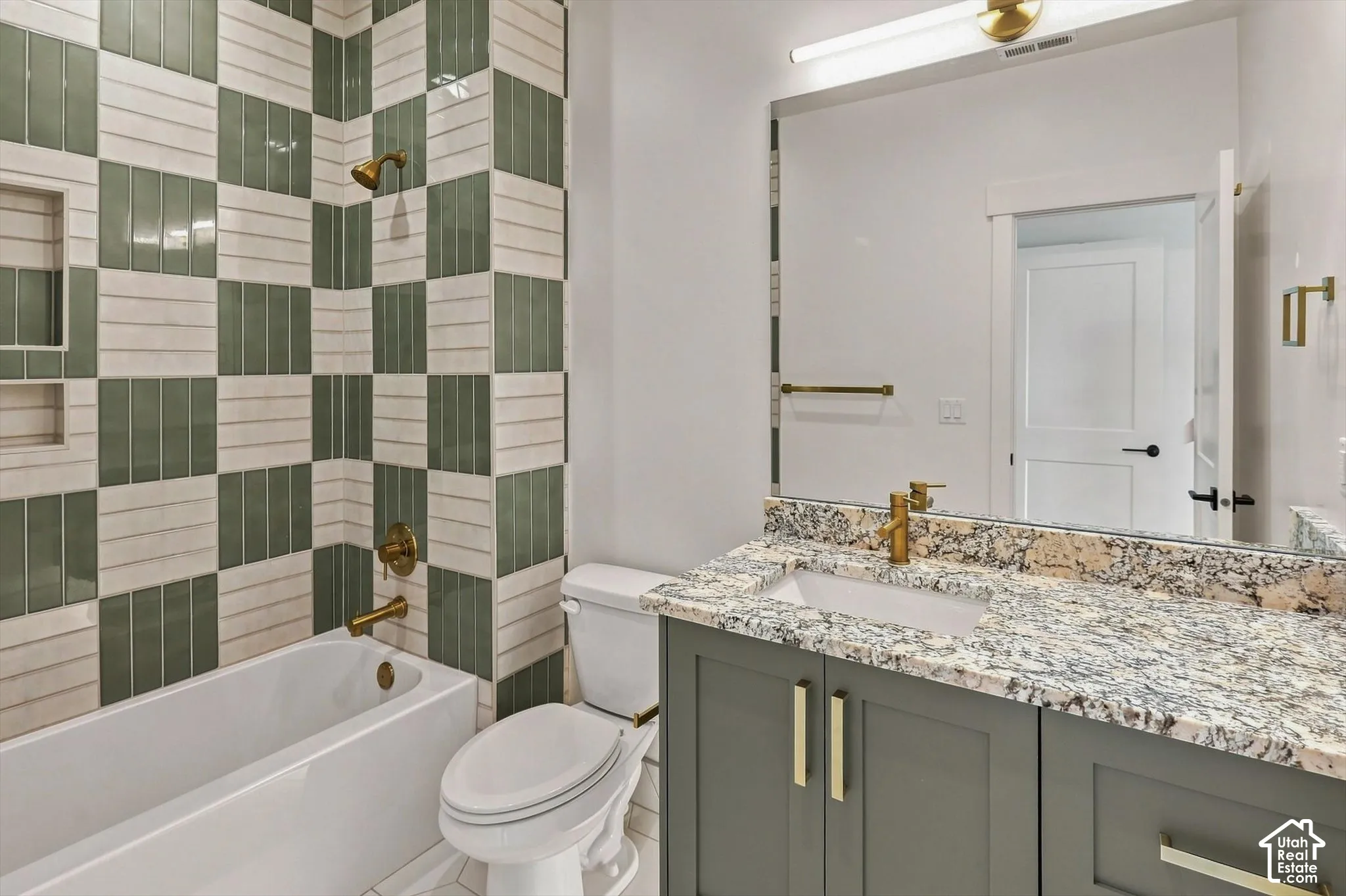 Bathroom featuring a checkered tile shower surround with integrated niche, white bathtub, single vanity with a granite countertop, undermount sink, and brass fixtures