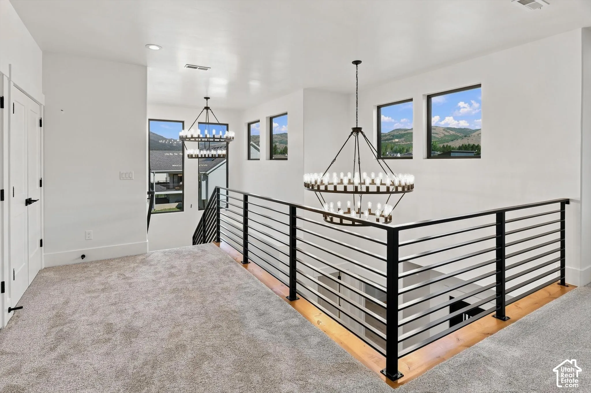 Carpeted landing with modern chandeliers, black metal horizontal bar railing, and multiple windows