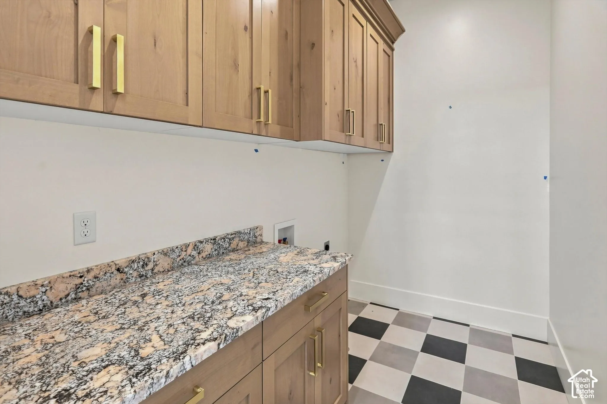 Light wood-finish cabinetry with gold hardware, granite-style countertop, and checkerboard floor tiling