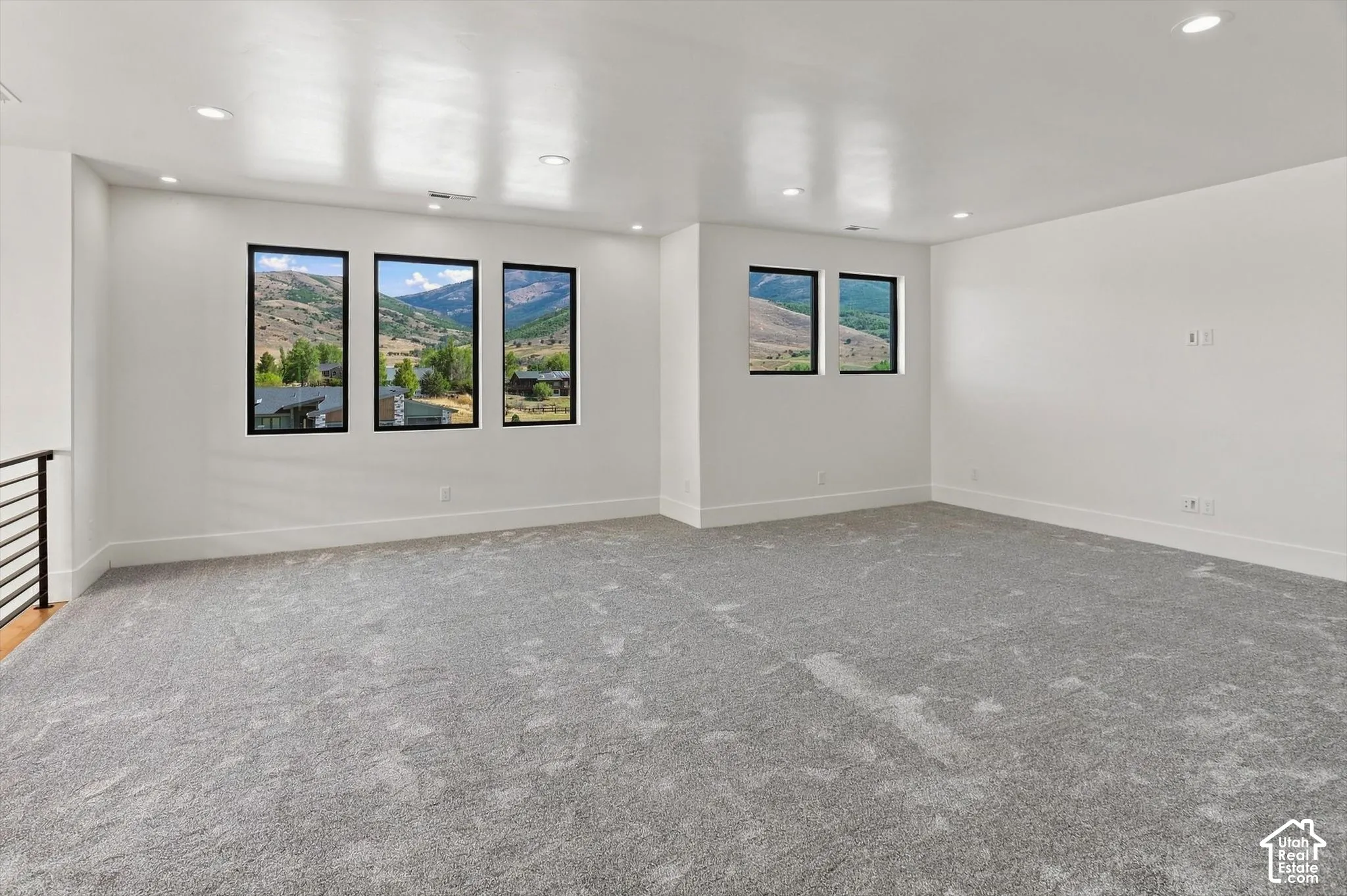 Spacious room featuring gray textured carpeting, white walls, recessed ceiling lighting, and multiple windows with black frames