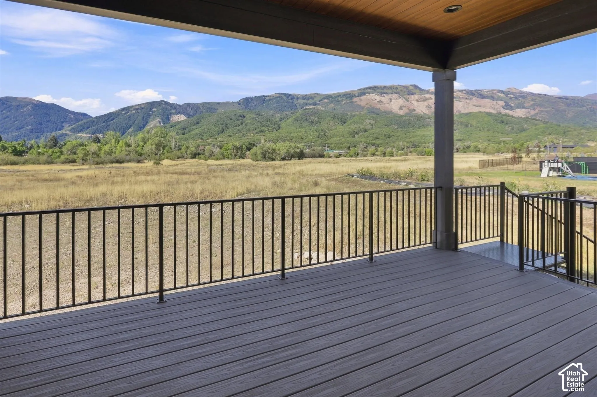 Expansive outdoor deck featuring composite decking, black metal railings, and a wood-finish ceiling with recessed lighting
