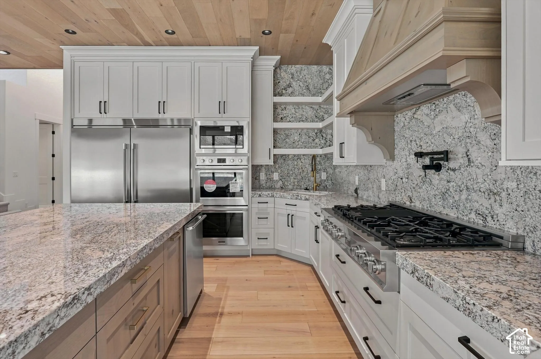 Kitchen featuring light wood-finish flooring, white cabinetry, integrated stainless steel appliances, granite countertops, and a wood-paneled ceiling