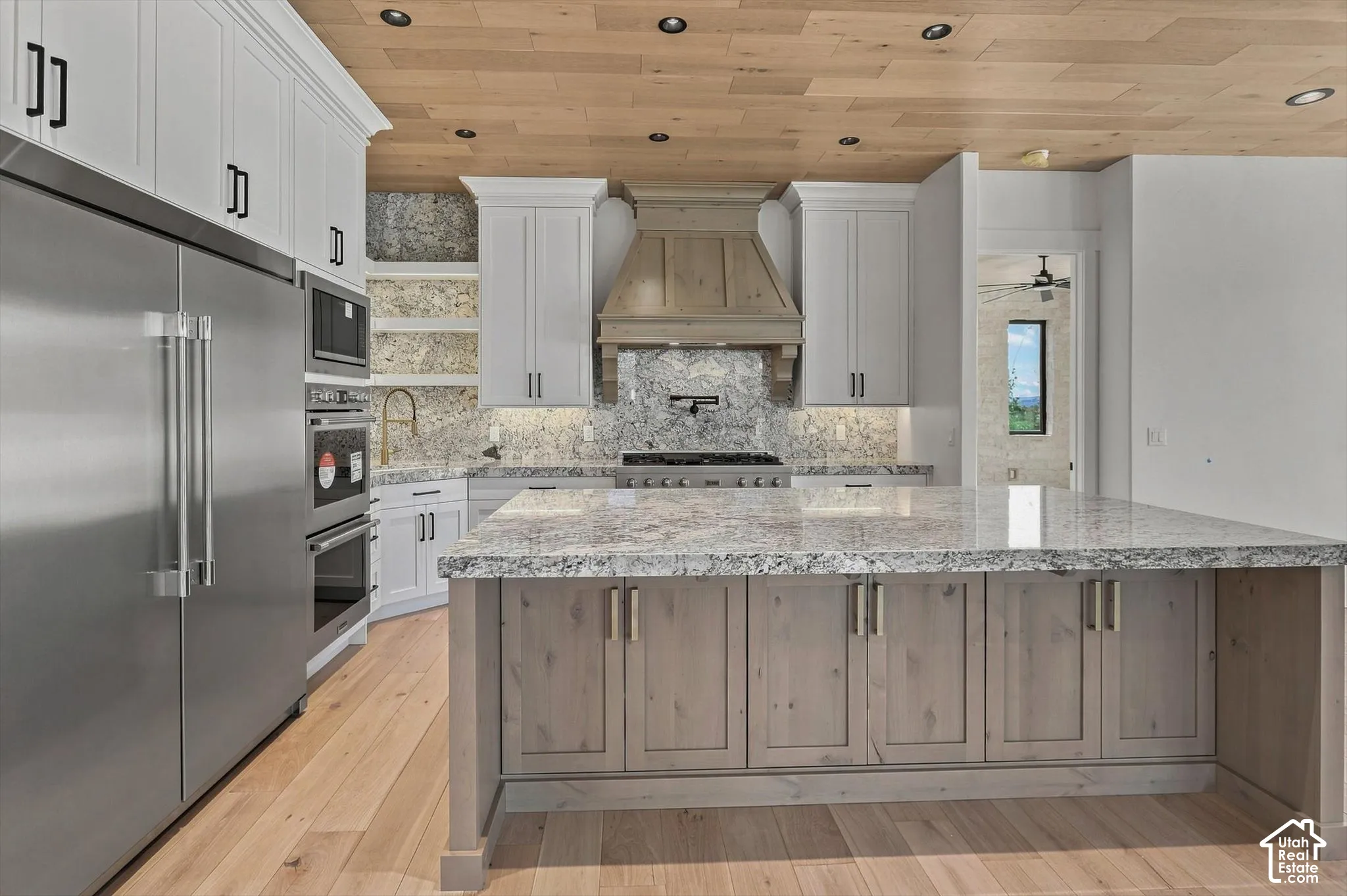 Hardwood flooring, stainless steel appliances, white perimeter cabinetry, stone countertops, and a wood-finish range hood