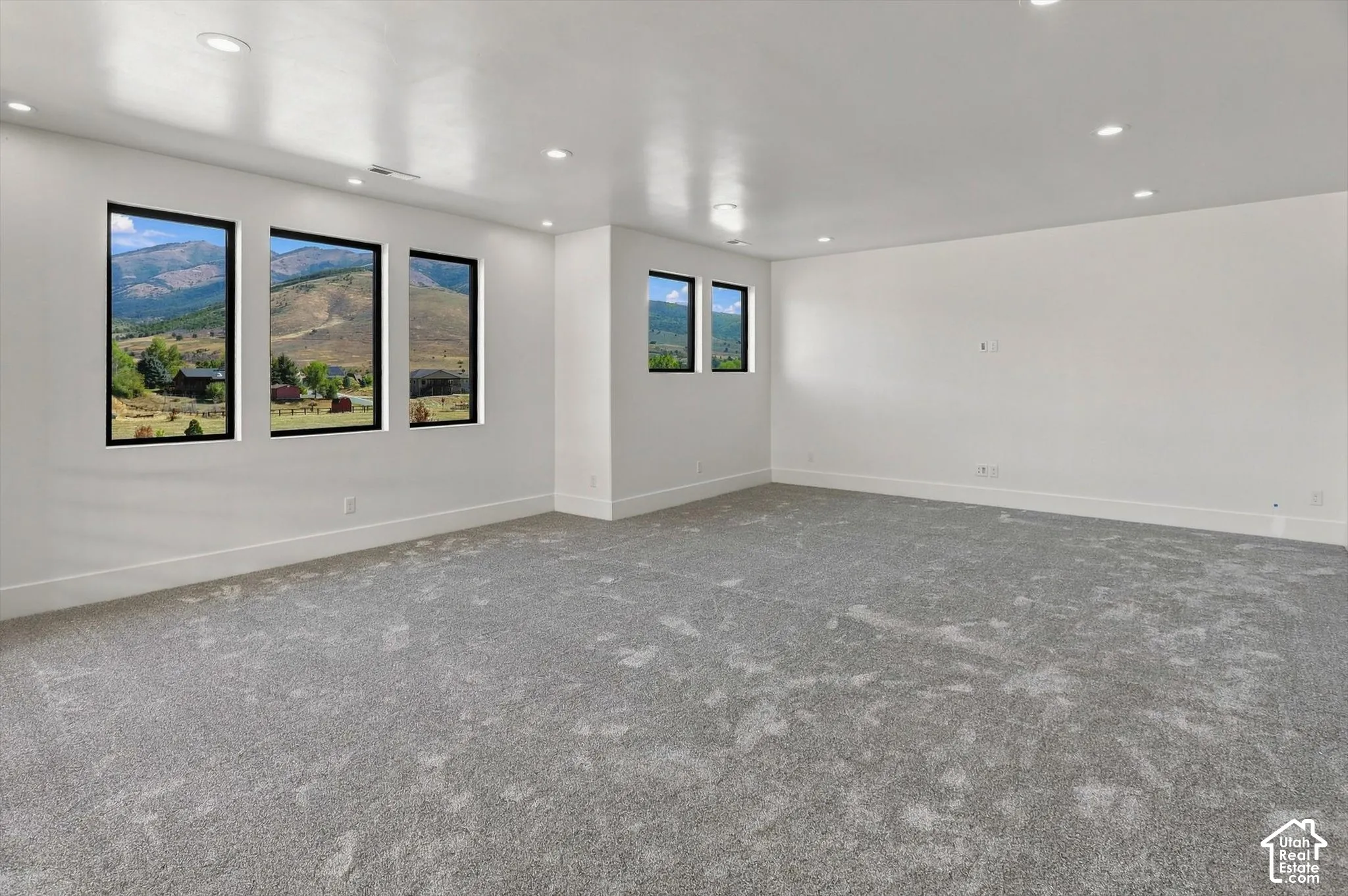 Recessed lighting, light gray carpeting, crisp white walls, multiple windows with black frames, and mountain scenery
